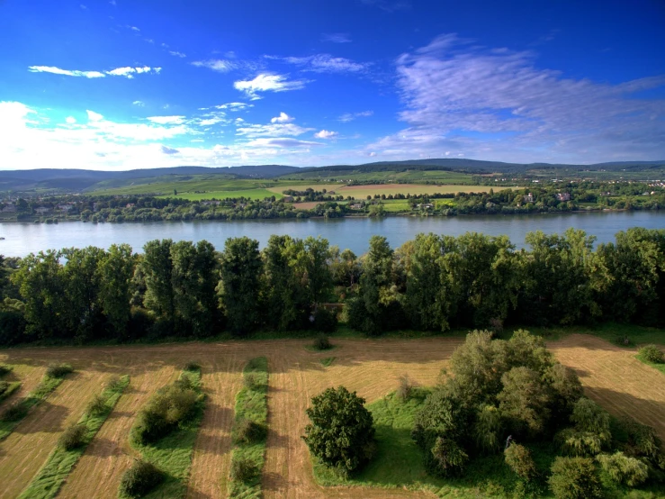 a large body of water surrounded by trees, by Karl Hagedorn, shutterstock, fields in foreground, wide river and lake, 8 k. filling of the view, ultra wide-shot