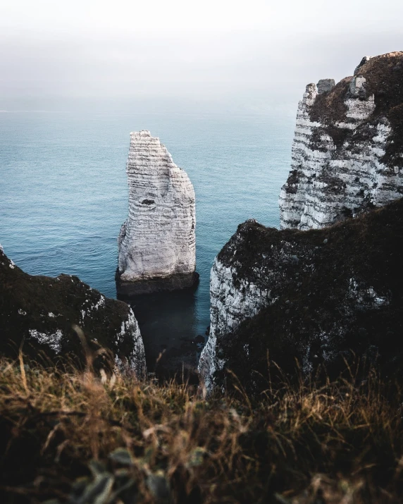 a rock formation in the middle of a body of water, by Raphaël Collin, pexels contest winner, cliffs of dover, northern france, 5 5 mm photo, grain”