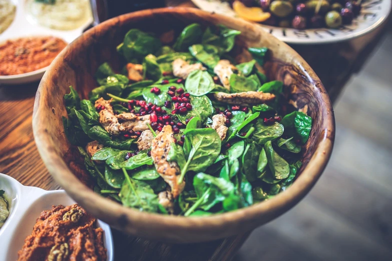 a wooden bowl sitting on top of a table filled with food, by Romain brook, pexels, salad, green and red tones, stock photo, eating meat