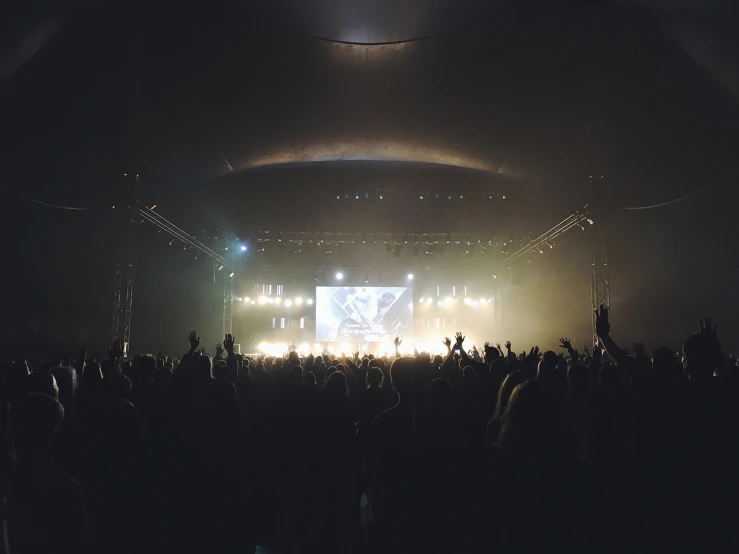 a crowd of people standing in front of a stage, a picture, pexels, light and space, concert footage, vsco, foggy ambience, wide-screen