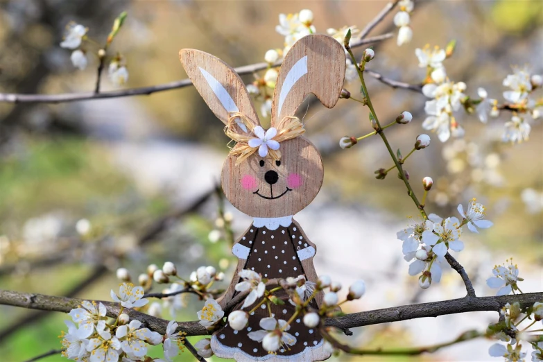 a wooden bunny sitting on top of a tree branch, a picture, pixabay, folk art, seasons!! : 🌸 ☀ 🍂 ❄, beautiful female, daisy, closeup photo