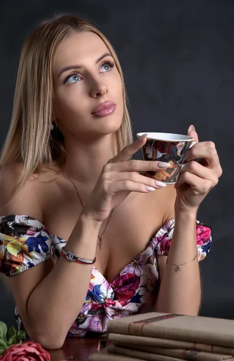 a woman sitting at a table holding a cup, a portrait, tumblr, blonde and attractive features, ukrainian girl, photo taken in 2 0 2 0, sexy :8