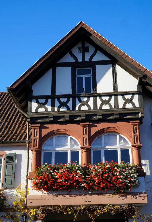 a house with a bunch of flowers on the balcony, by Karl Hagedorn, shutterstock, tudor architecture, red brown and white color scheme, sunny bay window, black forest
