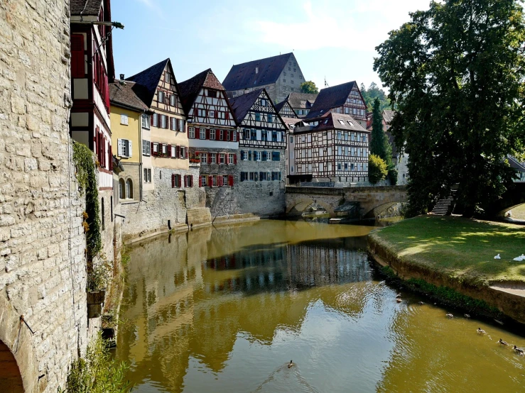 a river running through a city next to tall buildings, a picture, by Juergen von Huendeberg, flickr, renaissance, old village, black forest, beginning of autumn, slightly sunny weather