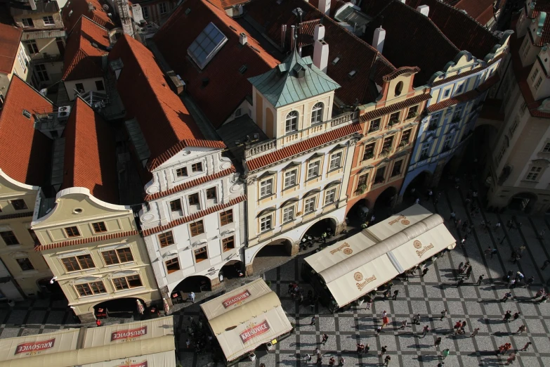 a group of people walking down a street next to tall buildings, a photo, by Josef Navrátil, pexels, art nouveau, viewed from bird's-eye, market square, colorful caparisons, prague