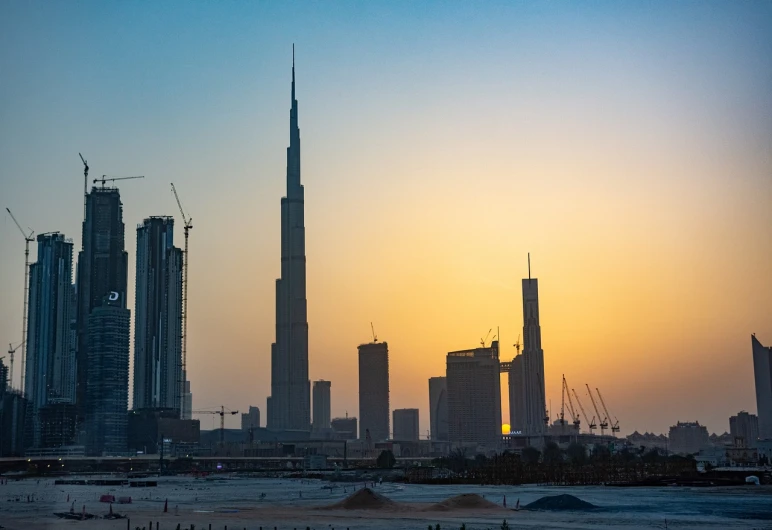 a group of people standing on top of a beach next to tall buildings, a stock photo, pexels contest winner, dau-al-set, sunset in the desert, construction, tall spires, 8k 50mm iso 10