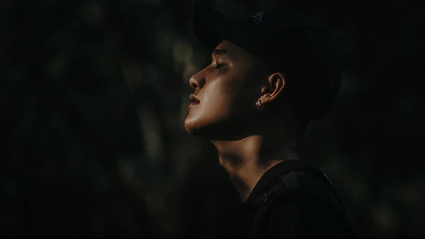 a close up of a person wearing a hat, inspired by Byron Galvez, unsplash contest winner, realism, in a dark forest low light, profile pose, asian male, official music video