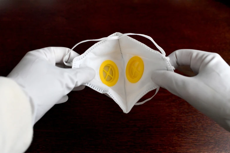 a person wearing white gloves and a face mask, a stock photo, by Dan Luvisi, bauhaus, yellow latex gloves, button eyes, close-up product photo, bag - valve mask