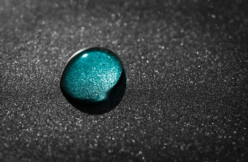 a blue stone sitting on top of a black surface, a macro photograph, minimalism, spraying liquid, emerald, with sparkling gems on top, shallow focus background