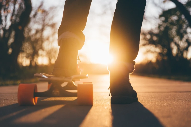 a person standing on top of a skateboard on a street, a picture, shutterstock, golden hour closeup photo, stock photo, slight lens flare, sunny amber morning light