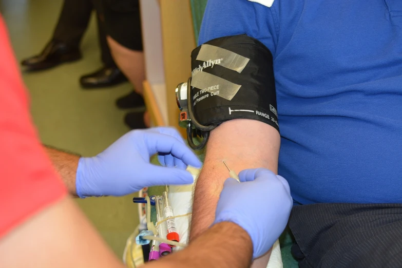 a person in a blue shirt is getting a blood test, by Dan Scott, happening, marsden, round-cropped, blog-photo, lots of detail