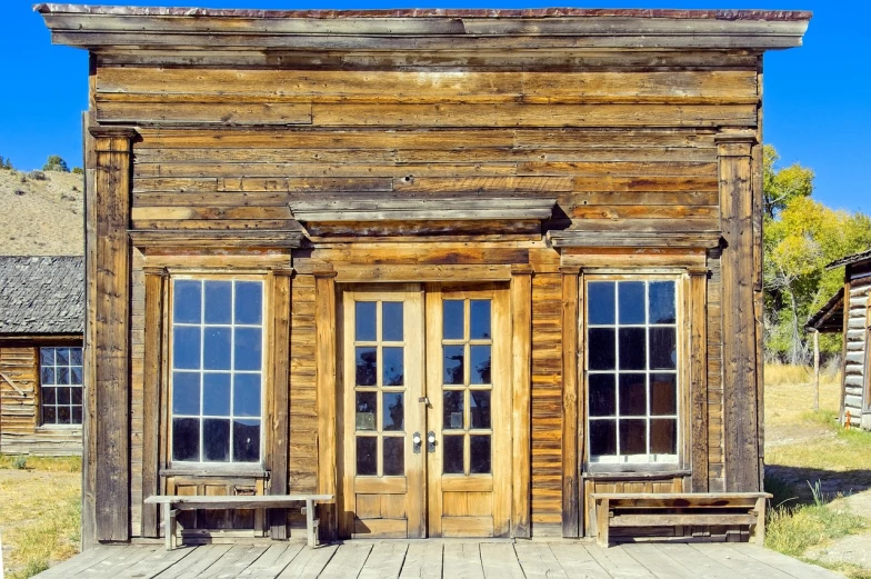 a wooden building with a bench in front of it, by Joseph Yoakum, shutterstock, oldwest, doors, overlooking, stock photo