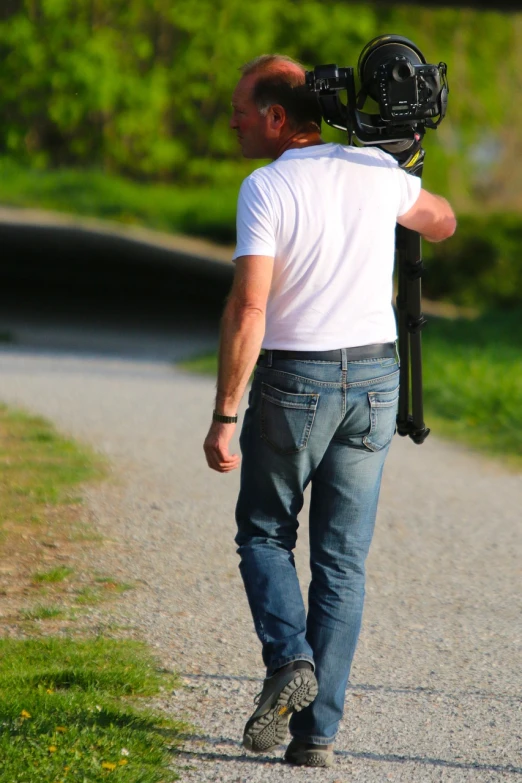 a man walking down a road holding a camera, plein air, jeans and t shirt, 1 3 5 mm!!, sniper! middle age man, dslr camera img_4016