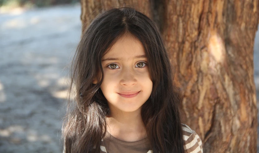 a young girl standing in front of a tree, by Lilia Alvarado, flickr, hurufiyya, black hair and large eyes, assyrian, smiling slightly, asher duran