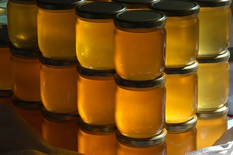 a stack of jars of honey sitting on top of a table, a picture, by Jan Rustem, jelly - like texture. photograph, las vegas, information, honeycomb structure