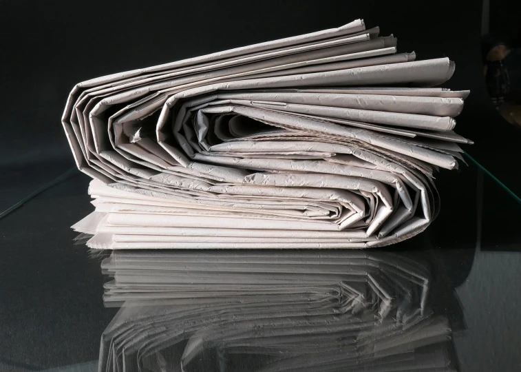 a stack of newspapers sitting on top of a table, a picture, by John Murdoch, with a black background, istockphoto, folds, reflection