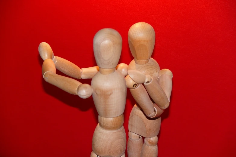 a couple of wooden mannequins standing next to each other, a picture, by Tom Carapic, in red background, reaching out to each other, playful composition canon, his back is turned