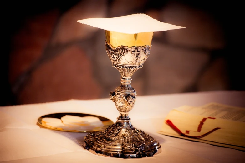 a silver cup sitting on top of a table next to an open book, sacrament, listing image, wine, lamp