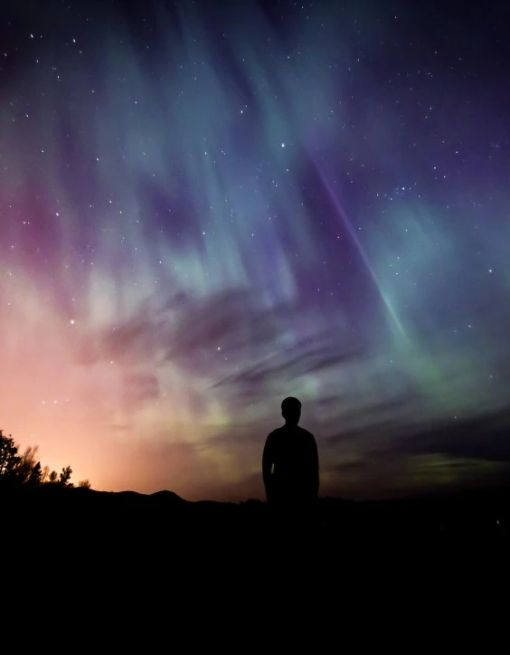 a man standing in front of a colorful sky, by Erwin Bowien, aurora, silhouette, northen lights background, very coherent image