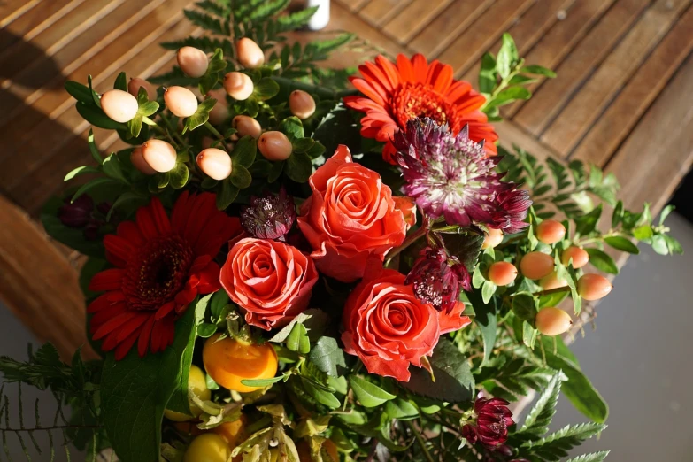 a bouquet of flowers sitting on top of a wooden table, inspired by François Boquet, realism, closeup - view, fruit and flowers, light red and deep orange mood, roses and lush fern flowers