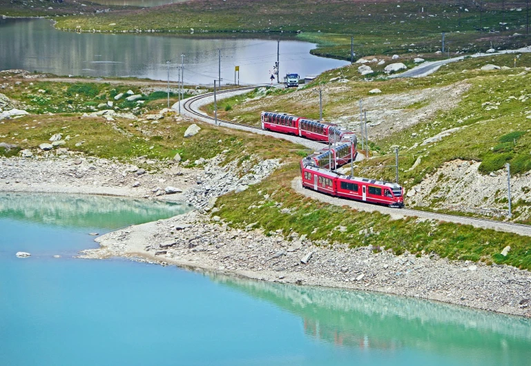 a red train traveling down tracks next to a body of water, a photo, by Werner Andermatt, shutterstock, trams, summer 2016, aerial shot, 1 1 1 1