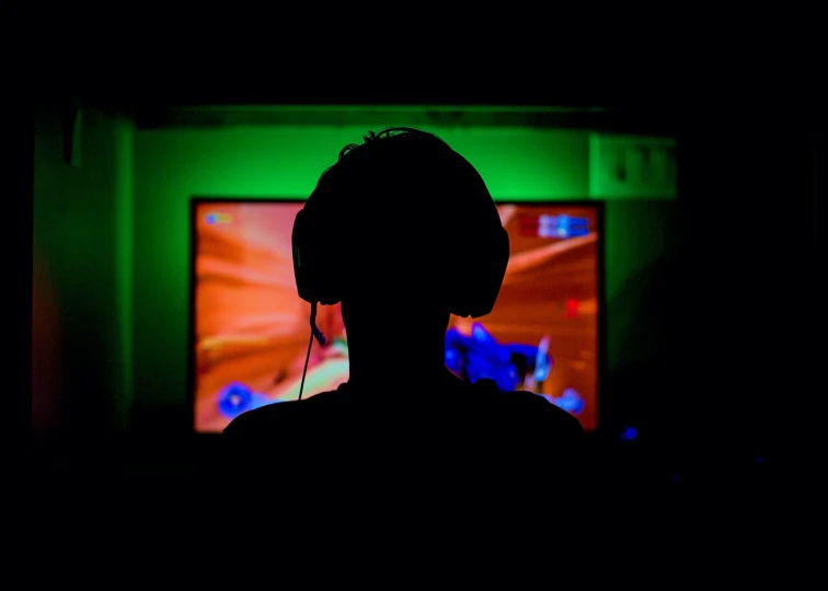 a silhouette of a person wearing headphones in front of a television, gaming computers, dramatic green lighting, game resources, colored lighting