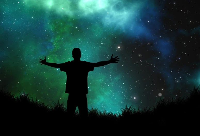 a man standing on top of a grass covered field, inspired by Aaron Douglas, shutterstock, digital art, dark neon colored universe, stock photo, stars in background, with arms up
