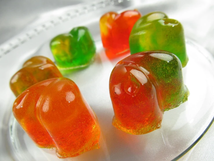 a group of gummy bears sitting on top of a glass plate, inspired by Władysław Podkowiński, dada, bright green dark orange, jelly - like texture. photograph, bells, high res