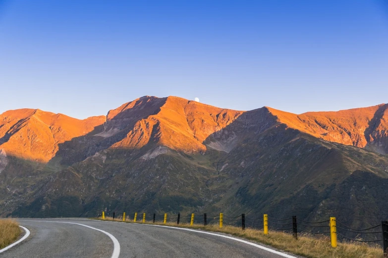 a curved road with mountains in the background, a picture, by Franz Hegi, shutterstock, late summer evening, new zeeland, details and vivid colors, pillar
