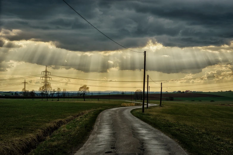 a dirt road in the middle of a field under a cloudy sky, a picture, by Hans Schwarz, pixabay contest winner, precisionism, shafts of light god rays, wires and lights, god rays pass through the window, some sun ray of lights falling