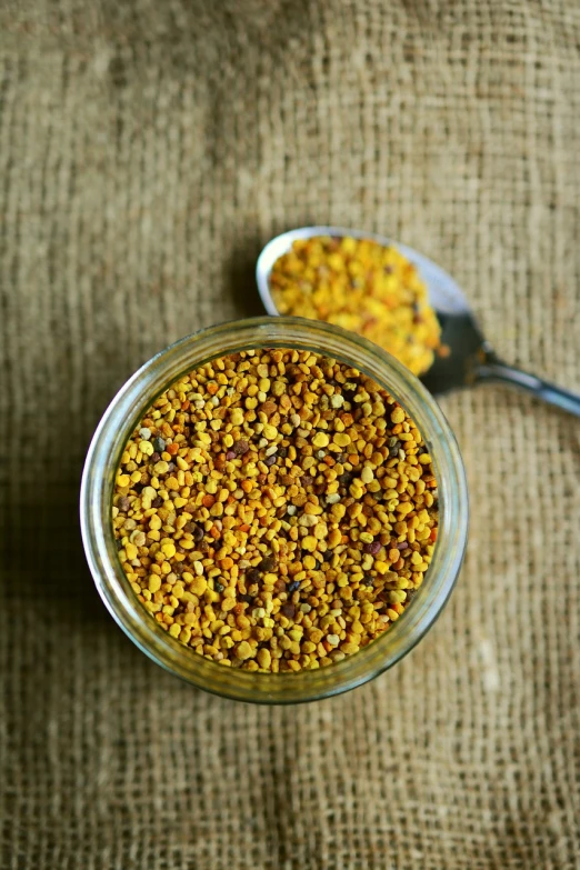 a glass jar filled with food next to a spoon, hurufiyya, pollen, yellow carpeted, buzzed sides, gold speckles