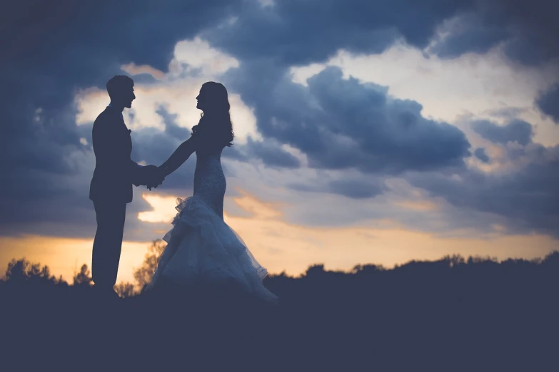 a bride and groom holding hands under a cloudy sky, pexels, romanticism, silhouette over sunset, istock, looking to the side, dimly - lit