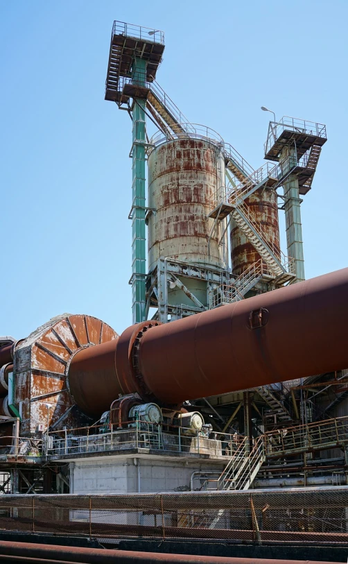 a large pipe sitting next to a train track, shutterstock, giant towering pillars, metal rust and plaster materials, on a sunny day, complex machinery