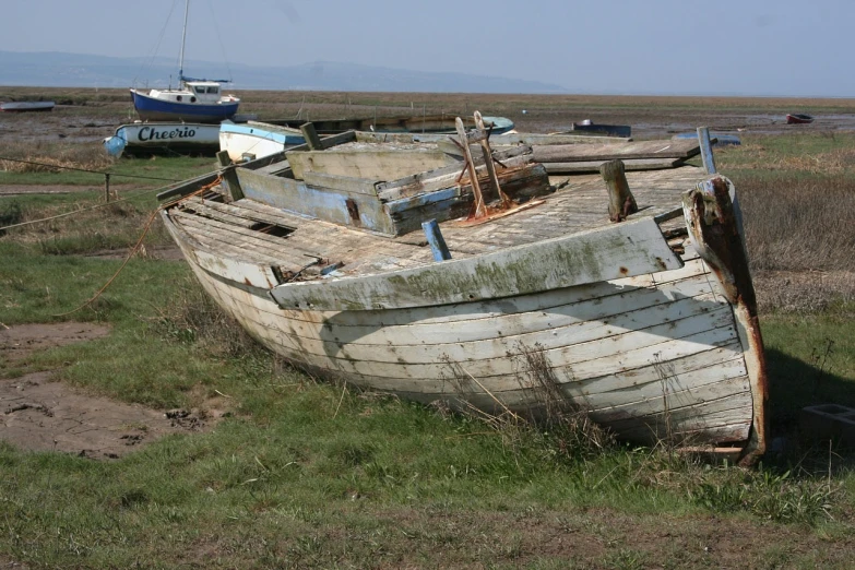 a wooden boat sitting on top of a grass covered field, by Richard Carline, flickr, land art, photo of poor condition, with water and boats, highfleet, on flickr in 2007