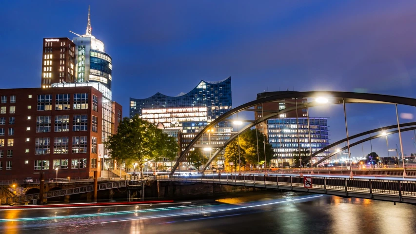 a bridge over a river in a city at night, a picture, inspired by Edwin Georgi, shutterstock, manchester, hannover, full of clear glass facades, late summer evening