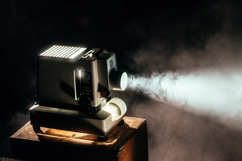 a projector sitting on top of a wooden table, by Werner Gutzeit, unsplash, video art, smoke machine, classic cinema, spotlight from above, film photo from 1970s