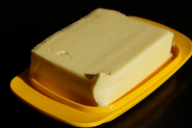 a piece of butter sitting on top of a yellow plate, a picture, by Dietmar Damerau, shutterstock, bauhaus, against a deep black background, in australia, perfect crisp sunlight, liquid that has a viscous