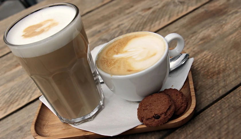 a cup of coffee and a cookie on a tray, iced latte, wikimedia commons, cappuccino, angled shot