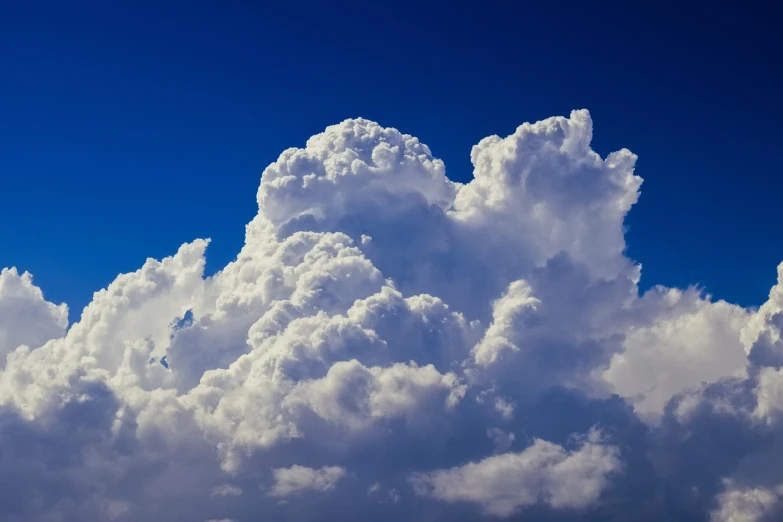 a plane flying through a cloud filled blue sky, a stock photo, minimalism, towering cumulonimbus clouds, white cyclops portrait in sky, vibrant vivid colors, giant cumulonimbus cloud