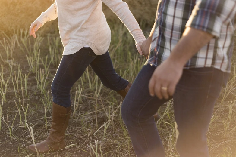 a man and a woman walking through a field, a picture, happening, wearing jeans, background image, loosely cropped, warm light