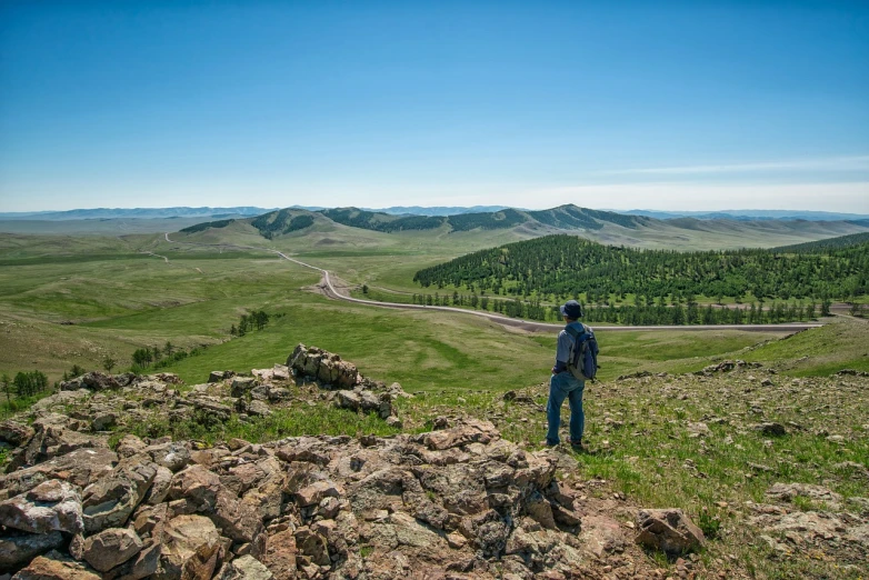 a person standing on top of a rocky hill, a portrait, mongol, tourist photo, meadows on hills, distant photo