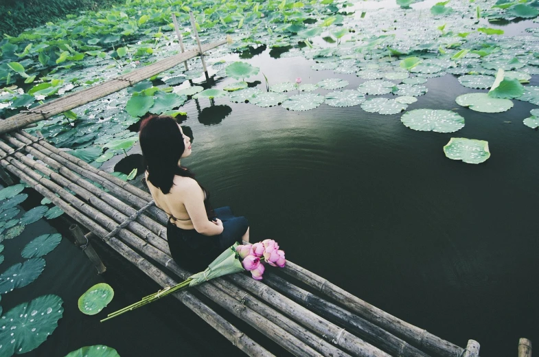 a woman sitting on a bamboo bridge next to a body of water, a picture, by Ju Lian, unsplash, happening, lillies, floating drowned, black lotus, beautiful lonely girl