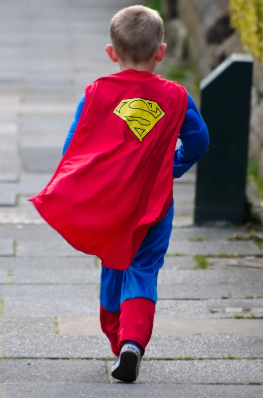 a young boy dressed in a superman costume, inspired by Norman Garstin, pexels, superflat, back towards camera, in a street, superior detail, heroism