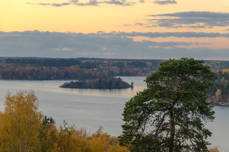 a large body of water surrounded by trees, a picture, by Johan Lundbye, shutterstock, stockholm, in the distance is a rocky hill, autumn sunset, tarmo juhola