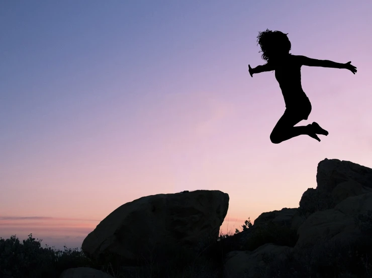 a silhouette of a person jumping in the air, on a rock, she expressing joy, header, getty images