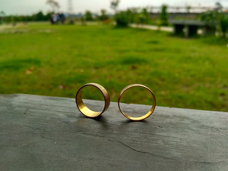 a couple of gold rings sitting on top of a wooden table, a picture, minimalism, at the park on a beautiful day, front side views full, captured on iphone, wedding photo