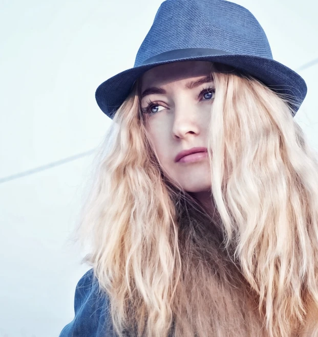 a woman with long blonde hair wearing a hat, by Zofia Stryjenska, shutterstock, blue coat, lorde, her hair is natural disheveled, matte detailed photo