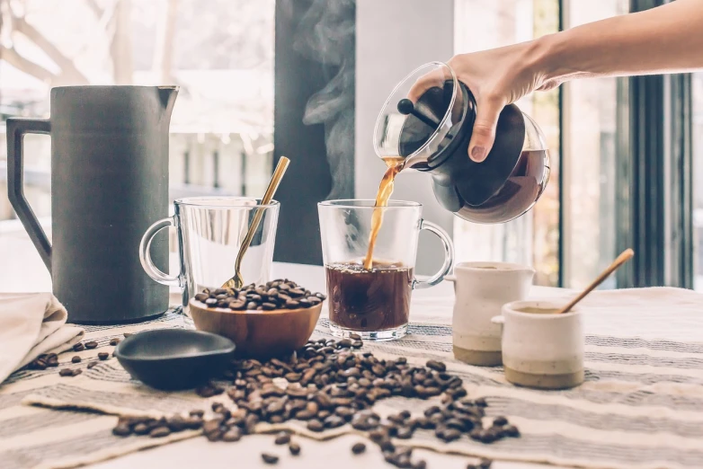 a person pouring a cup of coffee on a table, a still life, shutterstock, 🦩🪐🐞👩🏻🦳, beans, 7 0 mm photo, discovered photo