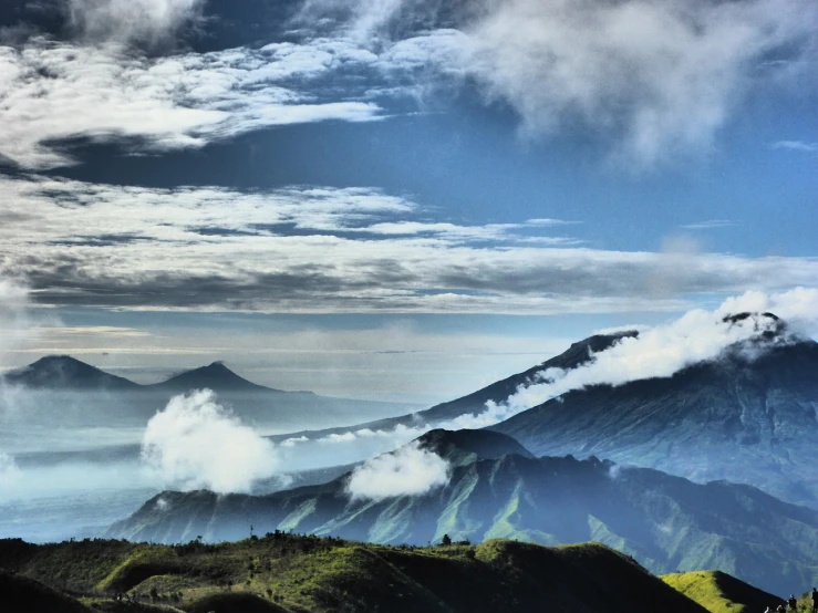 a group of people standing on top of a lush green hillside, a tilt shift photo, by Basuki Abdullah, flickr, sumatraism, volumetric clouds and fog, volcanic landscape, background image, hdr!