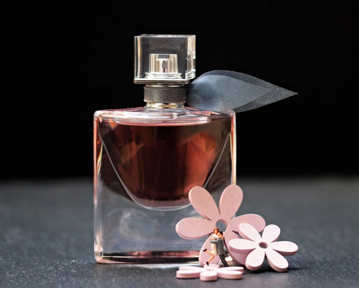 a bottle of perfume sitting on top of a table, a still life, by Zofia Stryjenska, pixabay, on a flat color black background, glass flowers, miniature product photo, brown and pink color scheme